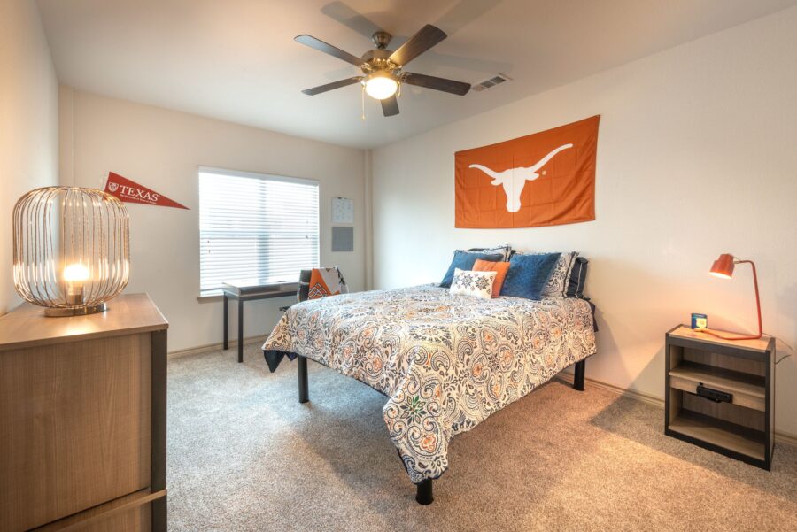 Alternate view of student apartment bedroom interior with University of Texas spirit decorations, full bed and walk-in closet with study desk and rolling chair