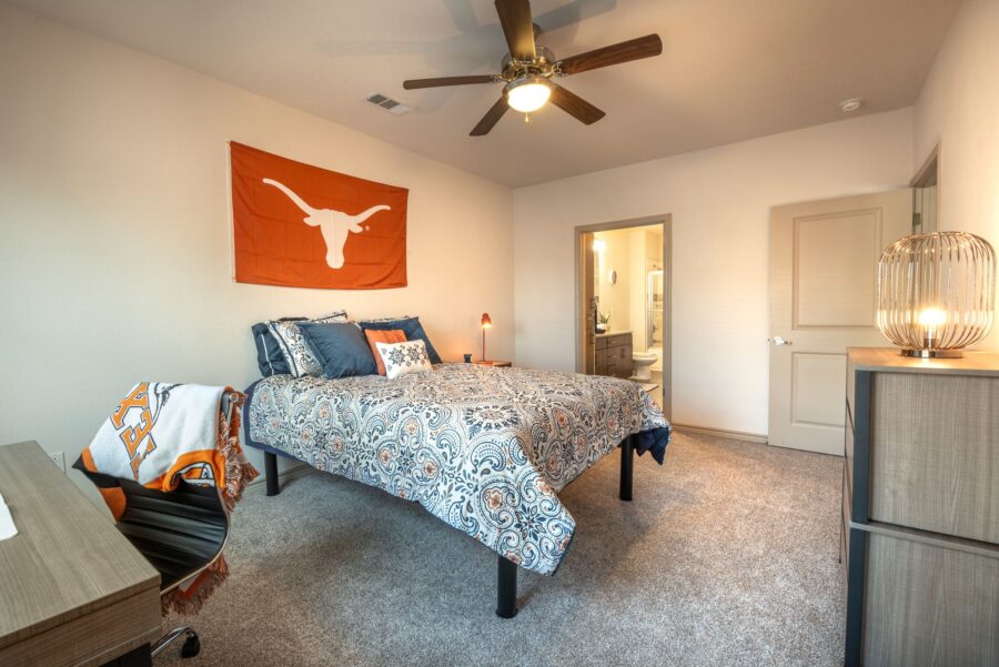 Interior of student apartment bedroom with University of Texas spirit decorations, full bed and walk-in closet with study desk and rolling chair