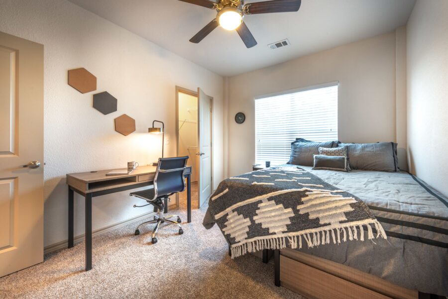Interior of student apartment bedroom with full bed and walk-in closet with study desk and rolling chair