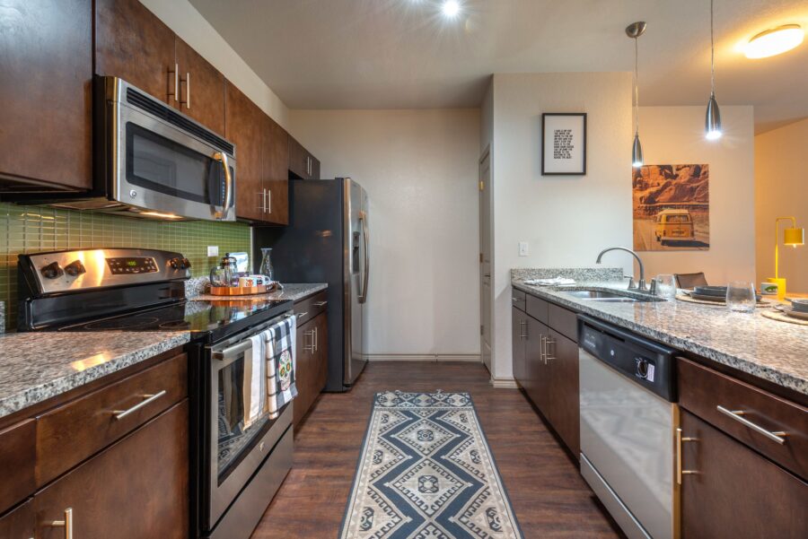 Apartment kitchen with stainless steel appliances, dishwasher, stove, microwave, granite countertops, wooden cabinets, and pantry