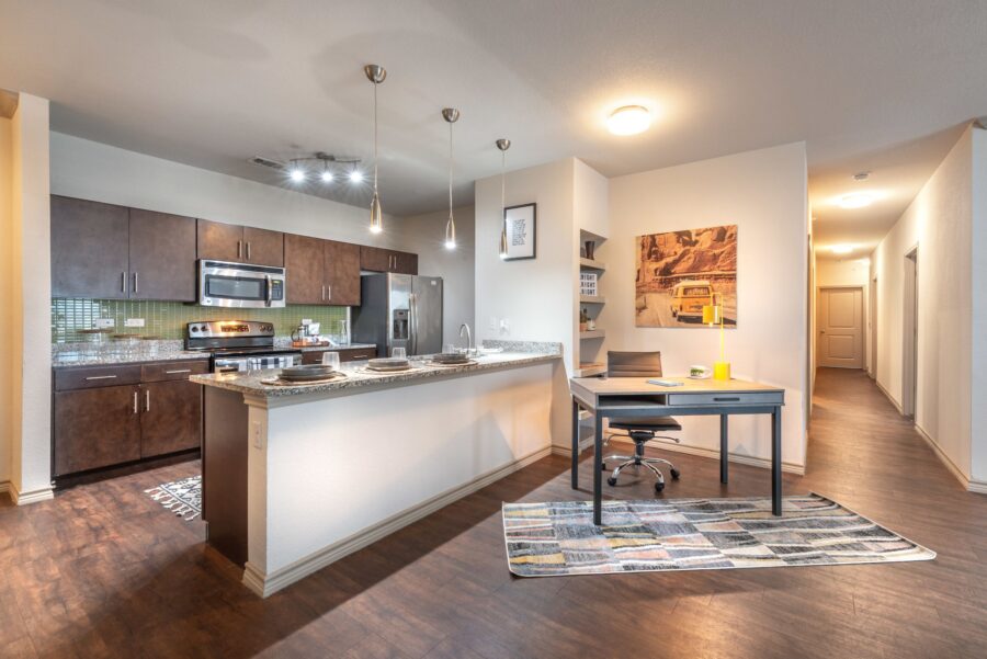 Interior of furnished apartment kitchen with granite counter, stainless steel appliances, and overhead lighting